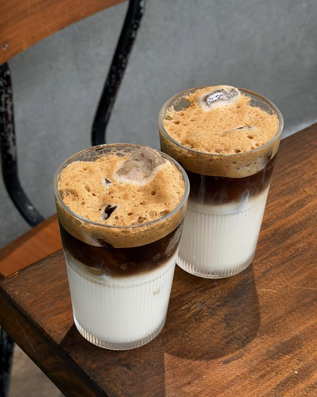 Two layered iced coffees with thick foam on a wooden table at The Hideout Café