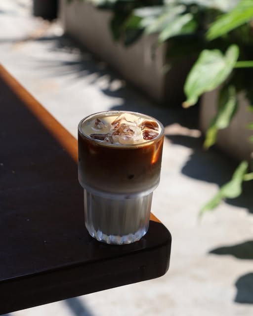 Iced coffee on an outdoor table in the sunlight beside green plants