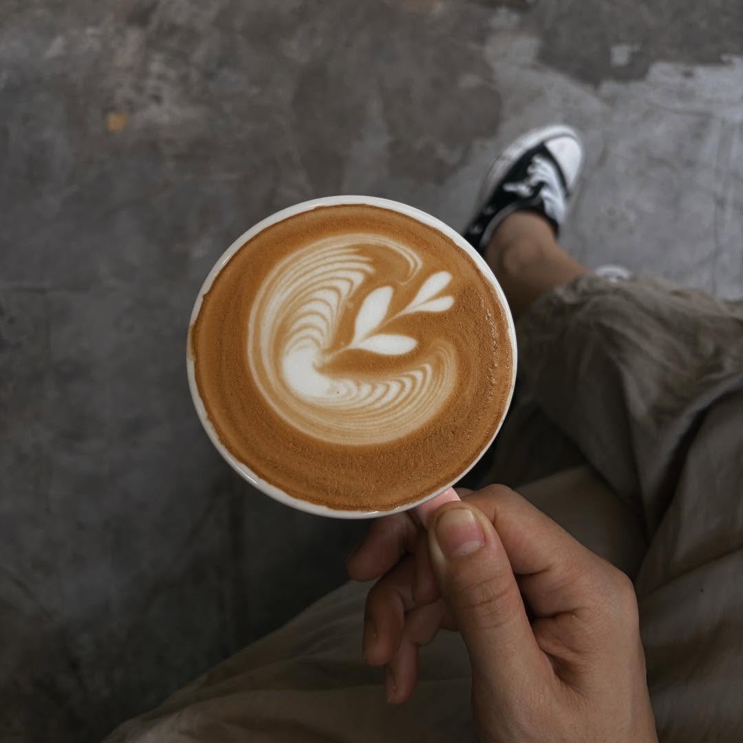 Cappuccino with latte art held over a concrete floor